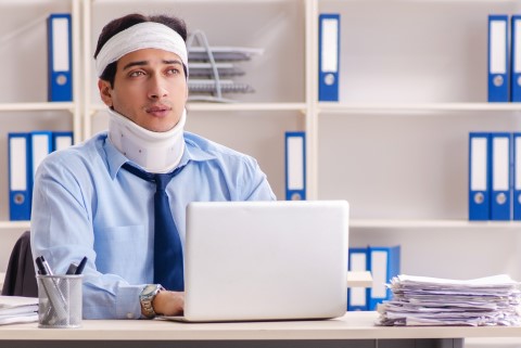 A you male worker having neck pain after a car accident with a neck brace on a laptop