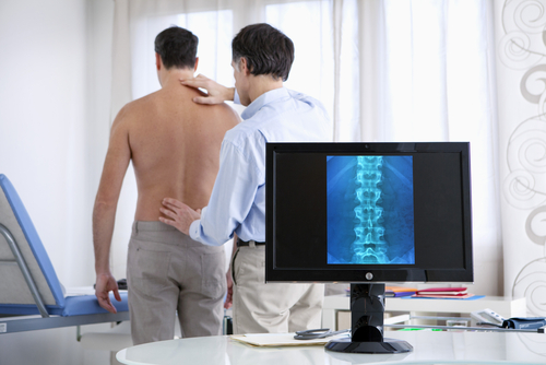 Doctor Examining Patient with Back Pain in Urgent Care Like Office Patient with lower back pain seeing a chiropractor instead of urgent care